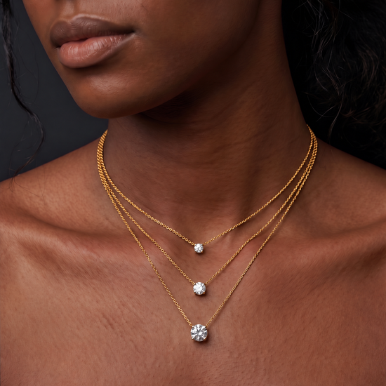 Diamond carat size comparison on a model's neck, showing 1-carat, 2-carat, and 3-carat round stones on a delicate three-tier layered gold chain necklace.