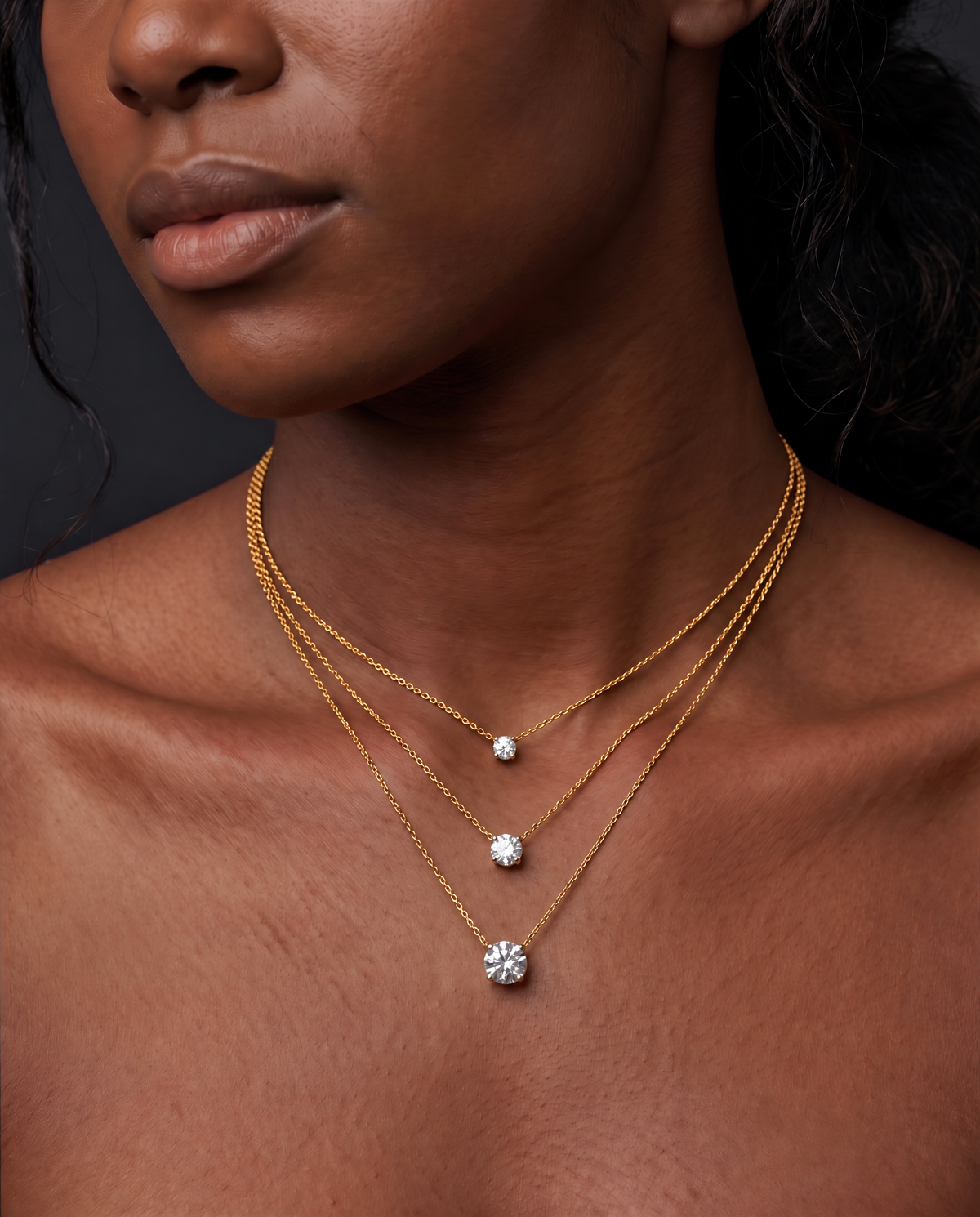Diamond carat size comparison on a model's neck, showing 1-carat, 2-carat, and 3-carat round stones on a delicate three-tier layered gold chain necklace.