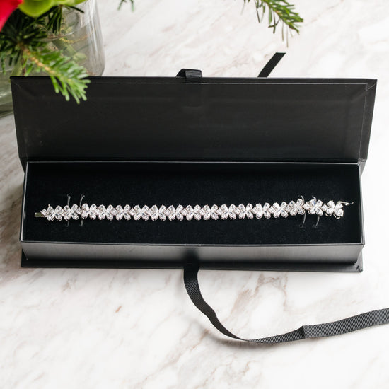 Top down view of a diamond floral tennis bracelet in white gold, featuring marquise and round diamonds arranged in repeating flower-inspired clusters with a flexible, high-polish setting.