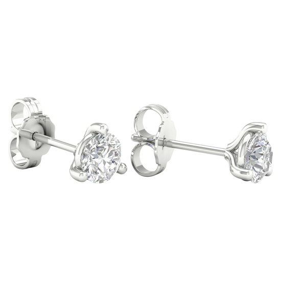 A pair of white gold or platinum stud earrings, each featuring a single brilliant-cut diamond held in a three-prong setting, displayed against a dark, transparent checkerboard background.