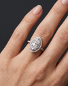 A close-up of a woman's hand elegantly displaying a large marquise-cut diamond ring with a double halo and a diamond-encrusted band. The ring rests naturally on her ring finger against a smooth, dark charcoal gray background. Soft, diffused lighting highlights the sparkling details of the jewelry and the natural texture of her skin, creating a luxurious and premium feel.