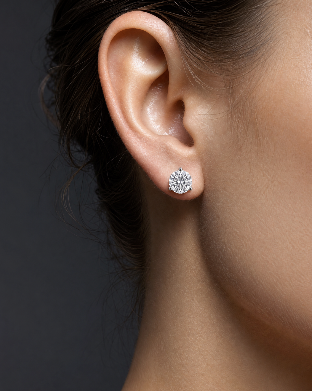 Profile view of a woman's ear wearing a round diamond stud earring.