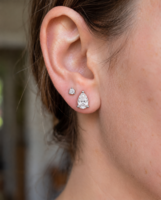Close-up profile of a model wearing a single pear-shaped diamond stud earring.