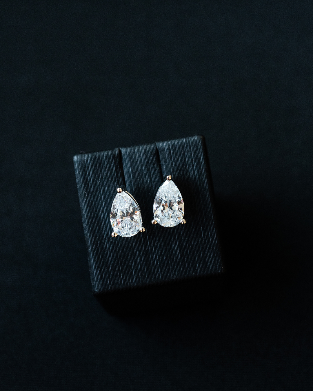 Amorati Diamonds Pear cut 6.0 total carat weight lab grown diamond stud earrings in black case and black background. 