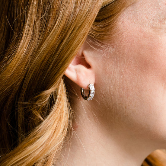 A pair of 14K white gold huggie hoops, shown from a side angle, highlighting the stacked diamonds and hinged closure on ear.