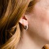 A pair of 14K white gold huggie hoops, shown from a side angle, highlighting the stacked diamonds and hinged closure on ear.