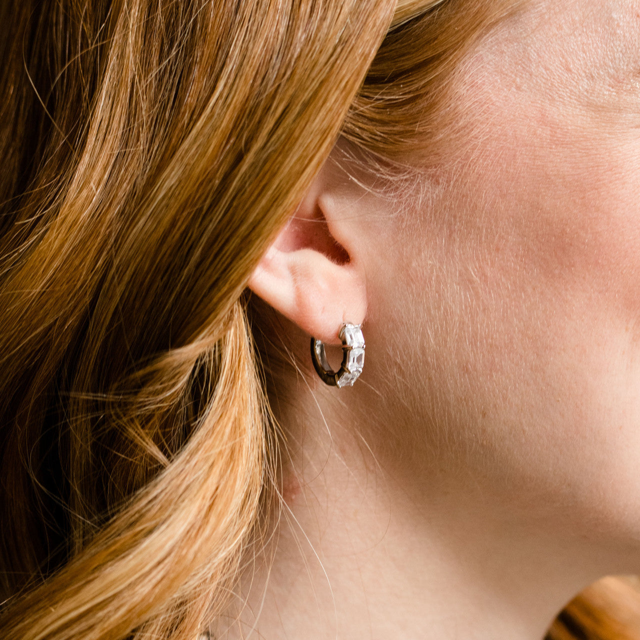 A pair of 14K white gold huggie hoops, shown from a side angle, highlighting the stacked diamonds and hinged closure on ear.