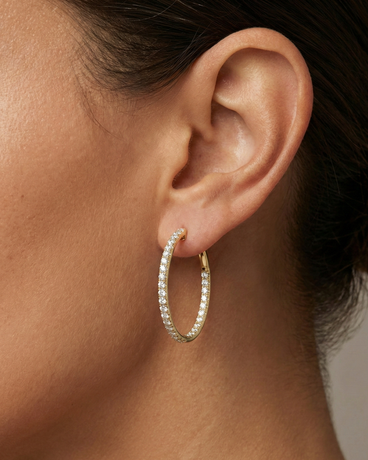 A pair of 14K yellow gold large hoop earrings, shown from a side angle, highlighting the line of diamonds and the hinged closure on hand.