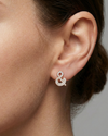 A pair of 14K yellow gold stud earrings shaped like an ampersand and covered in pavé diamonds, shown from the front on the ear.