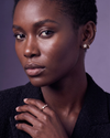 A Black woman wears a gold star diamond earring and a diamond trilogy ring against a lavender background.