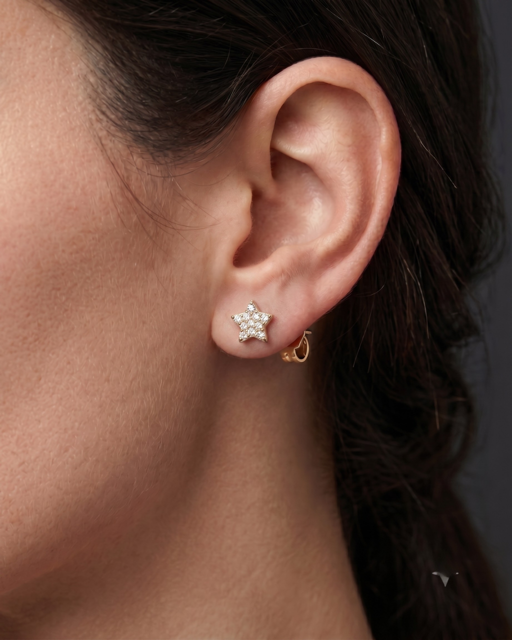A close-up photograph of a woman's ear wearing a single gold, star-shaped stud earring paved with diamonds.