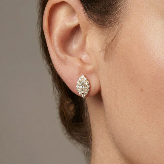 A pair of 14K yellow gold stud earrings with a marquise-shaped cluster of diamonds and a halo, shown from the front on ear.