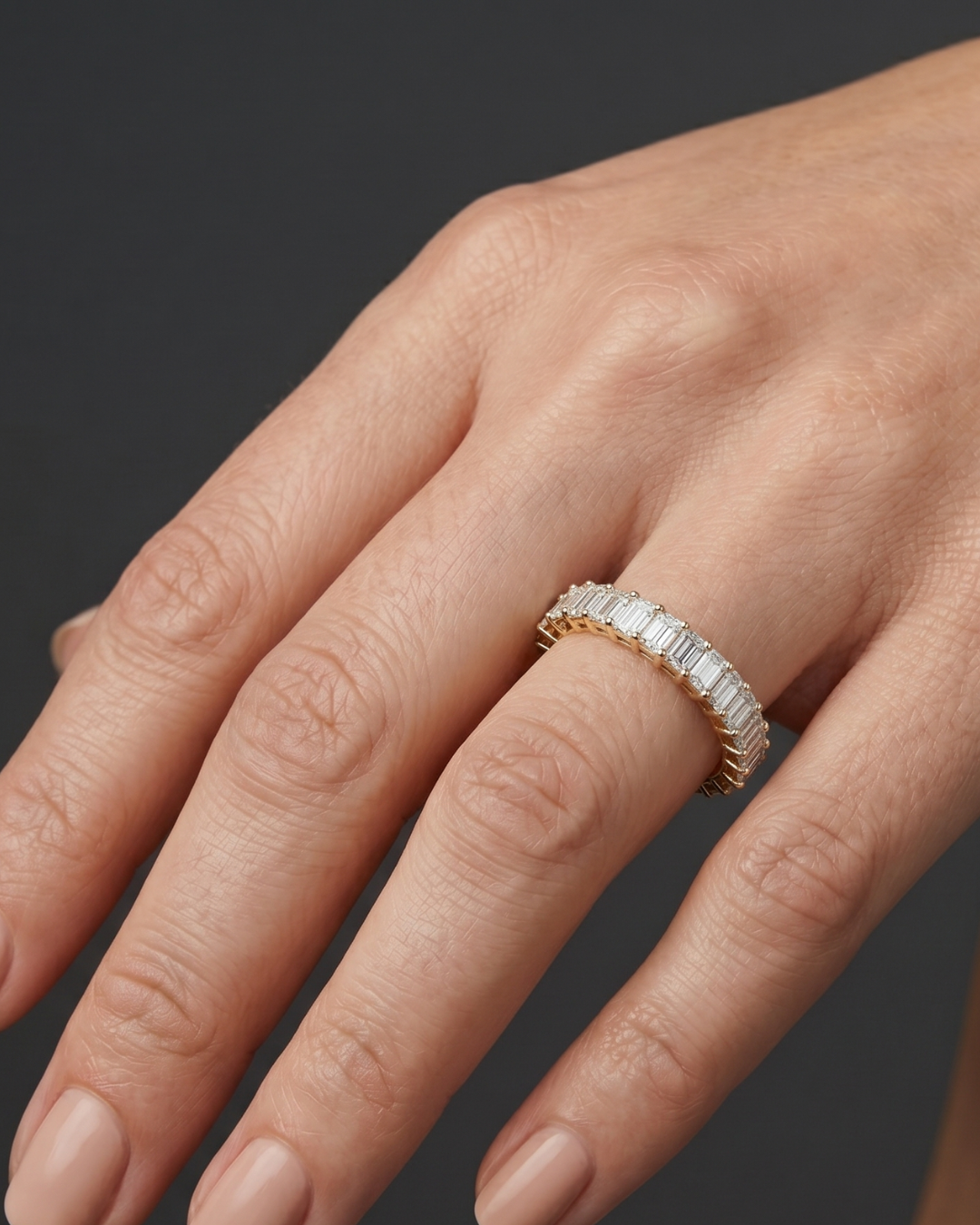 Lifestyle view of a model wearing a luxurious 14k yellow gold eternity ring fully set with a continuous row of shimmering emerald-cut diamonds.