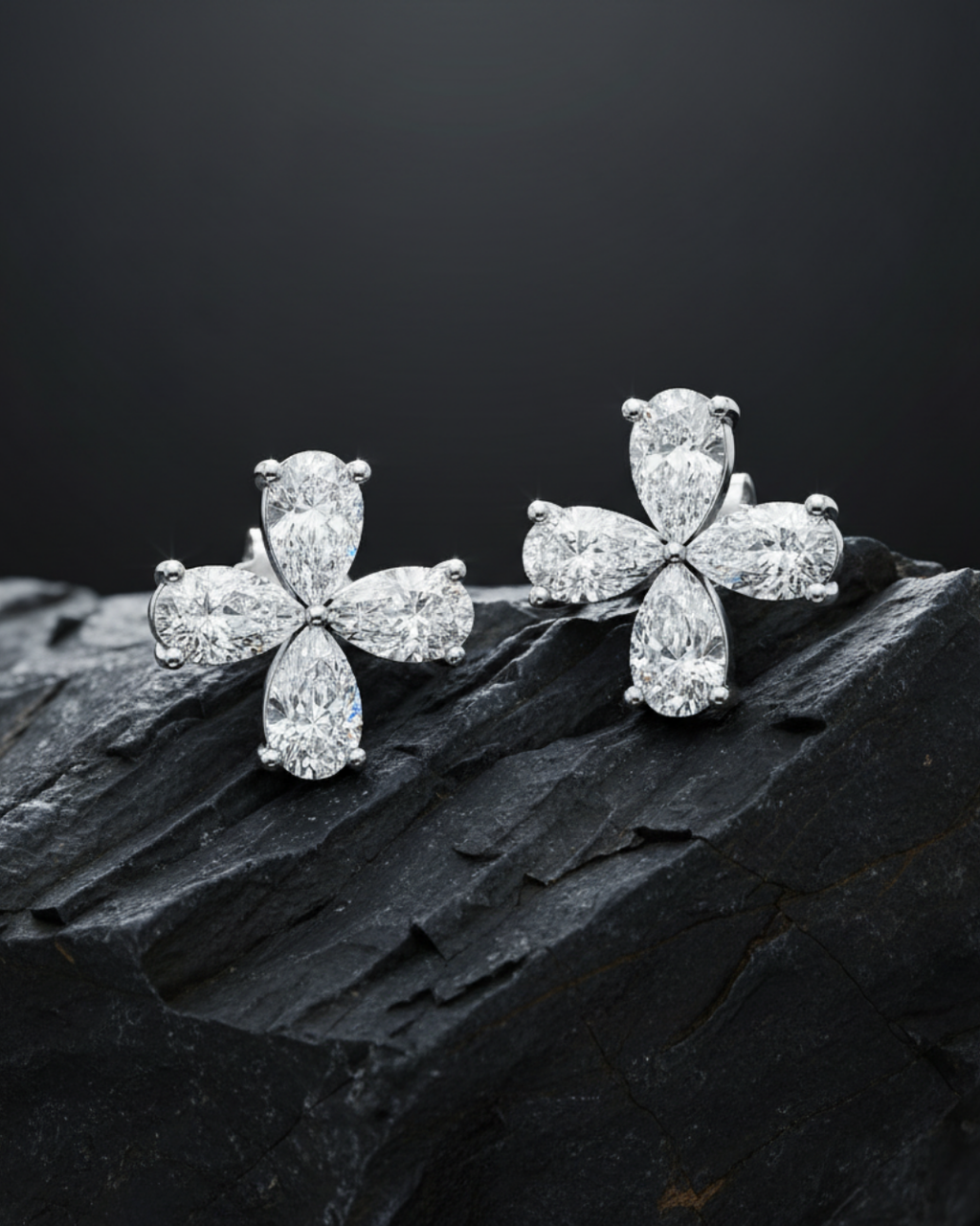 Two diamond flower studs are resting on a textured, dark gray rock to highlight their sparkle.