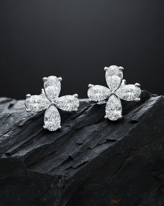 Two diamond flower studs are resting on a textured, dark gray rock to highlight their sparkle.