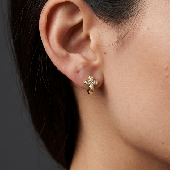 Close-up lifestyle view of a 14k yellow gold huggie earring featuring a prominent clover-shaped four-leaf flower motif studded with pear-cut white diamonds.