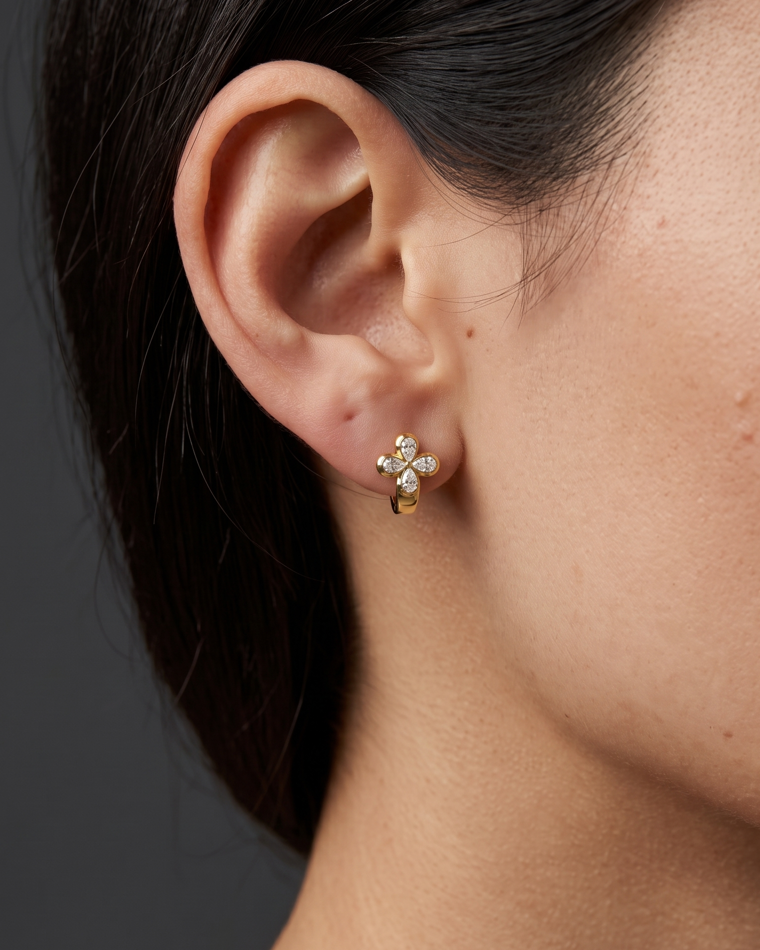 Close-up lifestyle view of a 14k yellow gold huggie earring featuring a prominent clover-shaped four-leaf flower motif studded with pear-cut white diamonds.