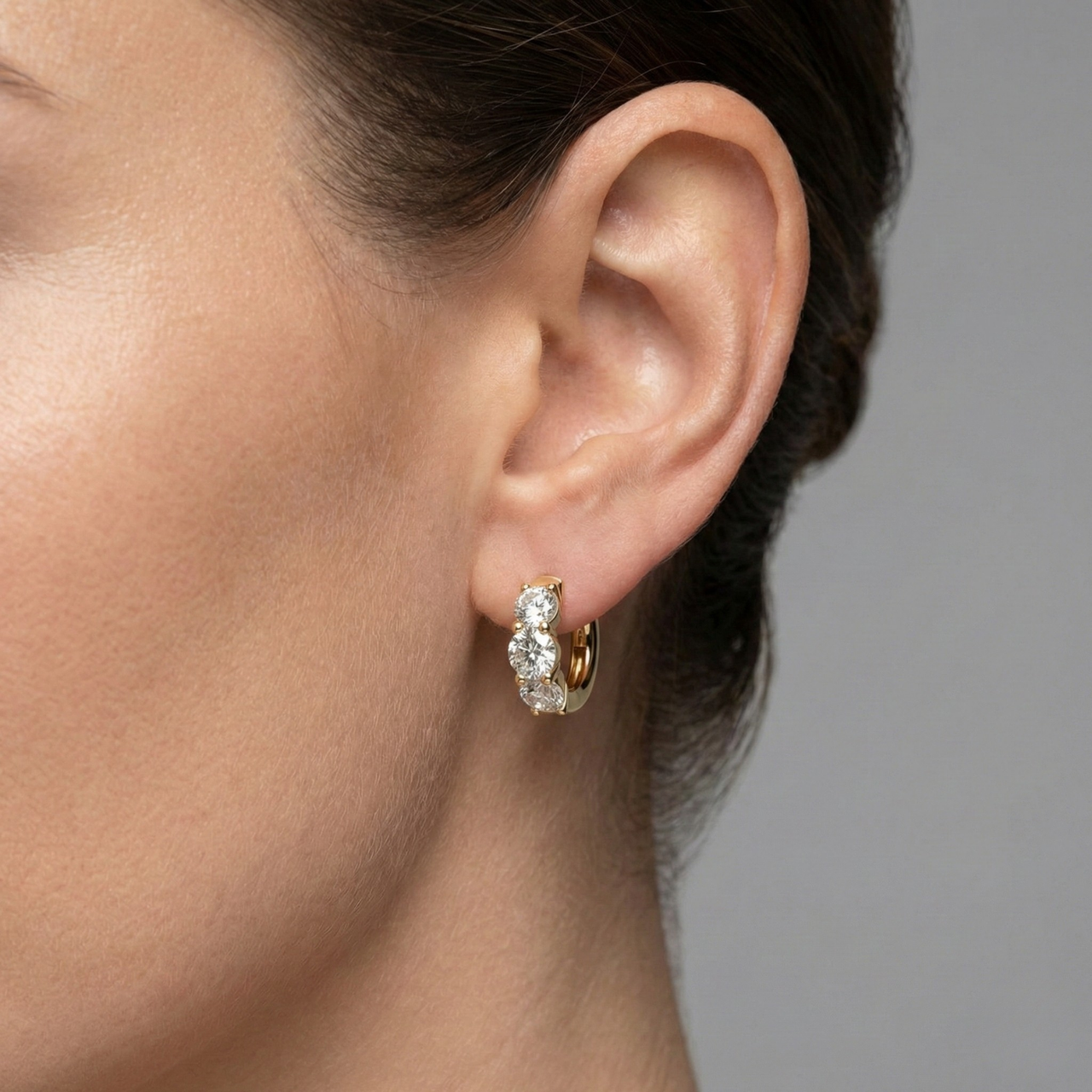 An angled view of a pair of 14K yellow gold huggie hoops, highlighting the wide, double-row design on ear.