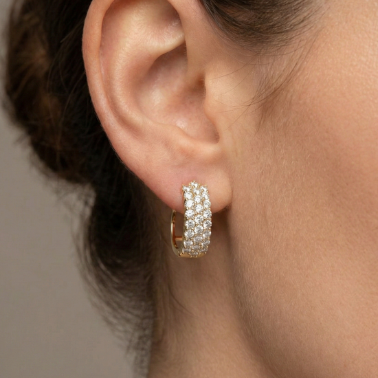 A pair of 14K yellow gold huggie hoops with three parallel rows of pavé diamonds, shown from the front on ear.
