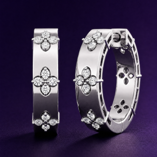 Close-up of Amorati white gold huggie earrings featuring diamond clover designs against a dark purple background.