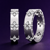 Close-up of Amorati white gold huggie earrings featuring diamond clover designs against a dark purple background.
