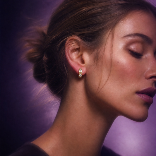 A model styled with Amorati yellow gold huggie hoop earrings. The jewelry features a repeating four-leaf clover pattern made of round diamonds.