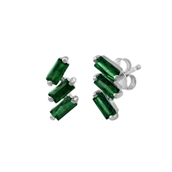 A pair of cascading stud earrings featuring a vertical arrangement of three baguette-cut emeralds in a deep, saturated green. The rectangular gemstones are staggered in a step-like formation and held in a minimalist 18k white gold setting, shown against a clean, white studio background.