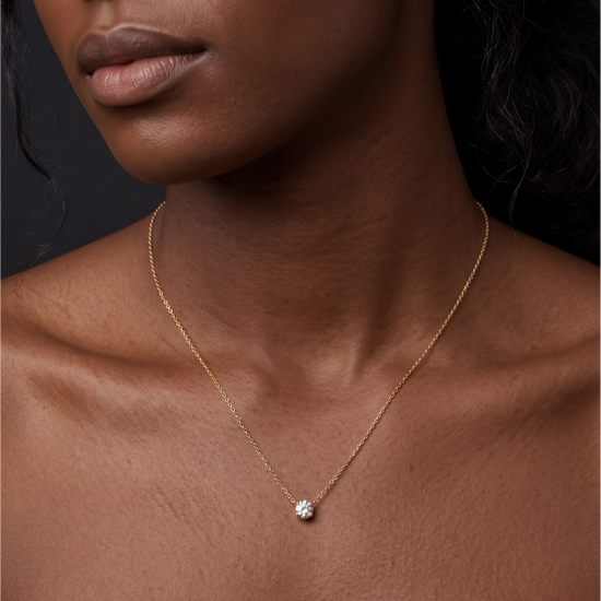 A close-up of a person's lower face and neck wearing a delicate yellow gold chain featuring a noticeably larger, single round 2-carat diamond pendant resting just below the collarbone.
