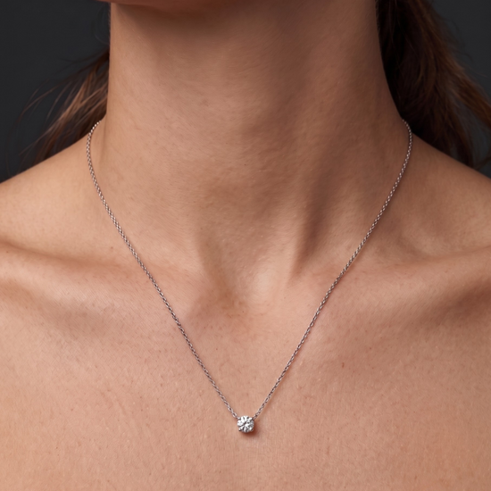 A close-up of a person wearing a delicate white gold chain necklace with a single round diamond pendant 1 carat. 