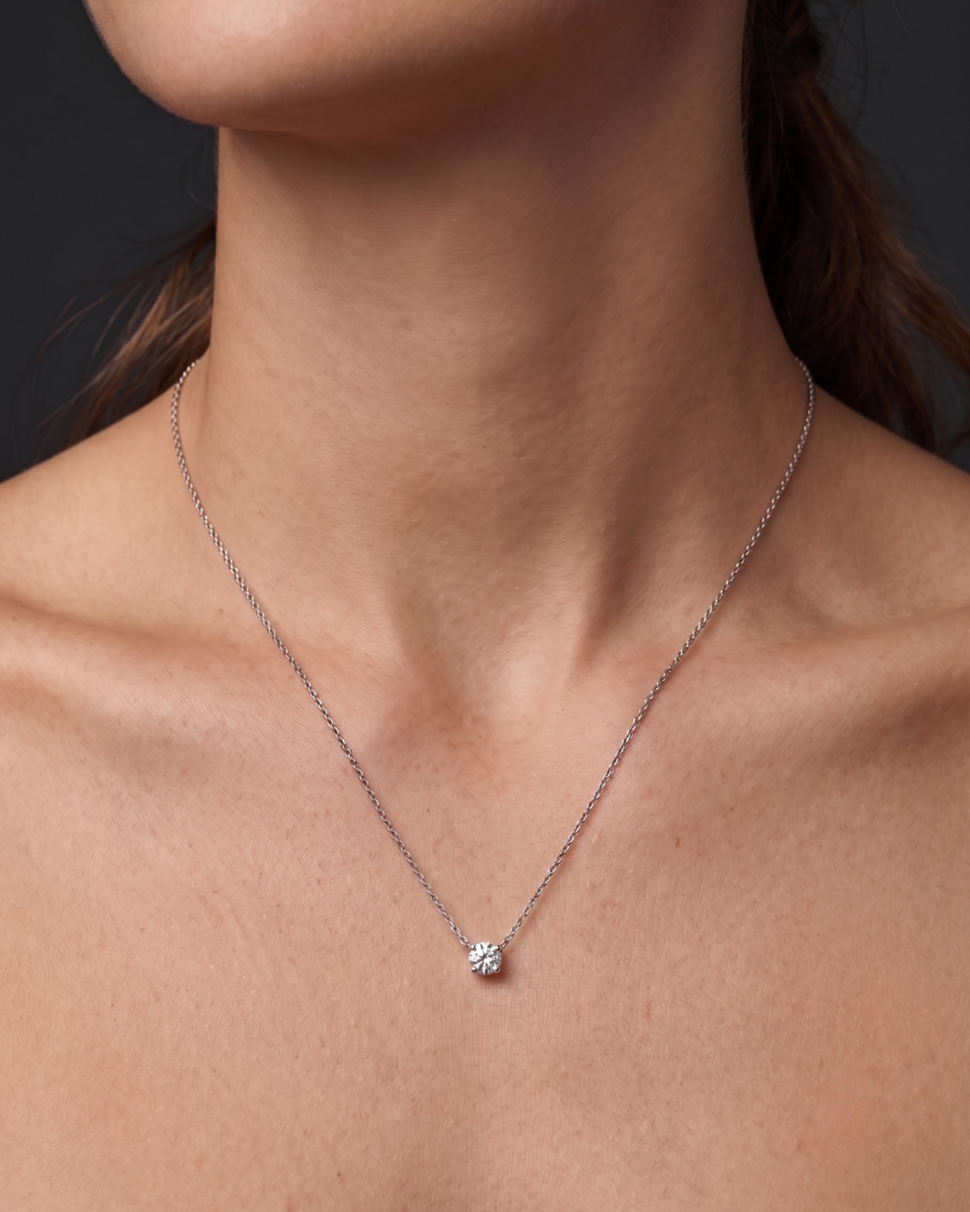 A close-up of a person wearing a delicate white gold chain necklace with a single round diamond pendant 1 carat. 