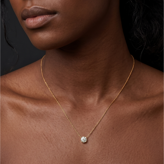 A close-up of a person's lower face and neck wearing a delicate yellow gold chain featuring a small, single round 1-carat diamond pendant resting just below the collarbone.