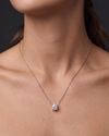 A close-up of a person wearing a delicate white gold chain necklace with a single round diamond pendant 2 carat. 