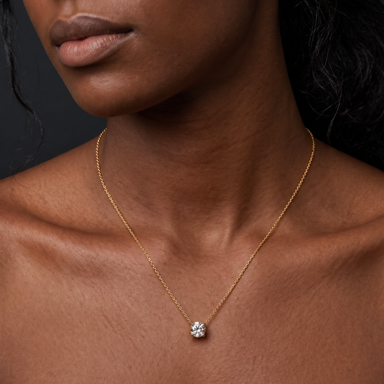 A close-up of a person's lower face and neck wearing a delicate yellow gold chain featuring a large, prominent single round 3-carat diamond pendant resting just below the collarbone.