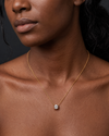 A close-up of a person's lower face and neck wearing a delicate yellow gold chain featuring a large, prominent single round 3-carat diamond pendant resting just below the collarbone.