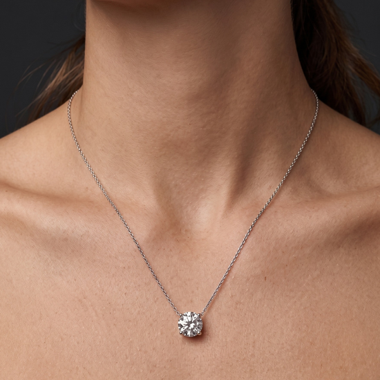 A close-up of a person wearing a delicate white gold chain necklace with a single round diamond pendant 3 carat. 
