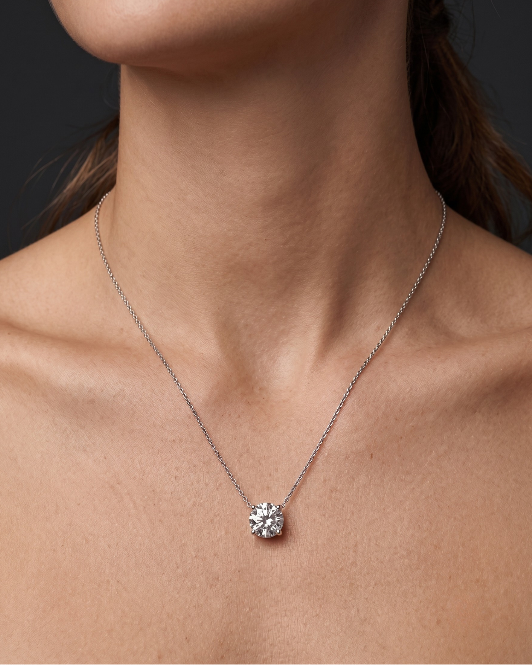 A close-up of a person wearing a delicate white gold chain necklace with a single round diamond pendant 3 carat. 