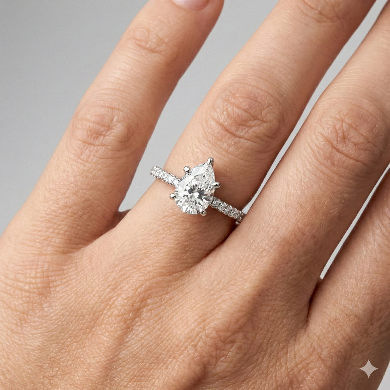 Pear cut diamond engagement ring in 14k white gold with a pavé diamond band and cathedral setting on a hand.