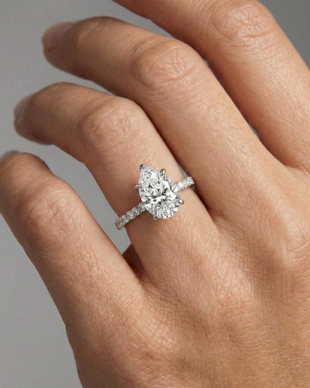Pear cut diamond engagement ring in 14k white gold with a prong diamond band and cathedral setting on a hand