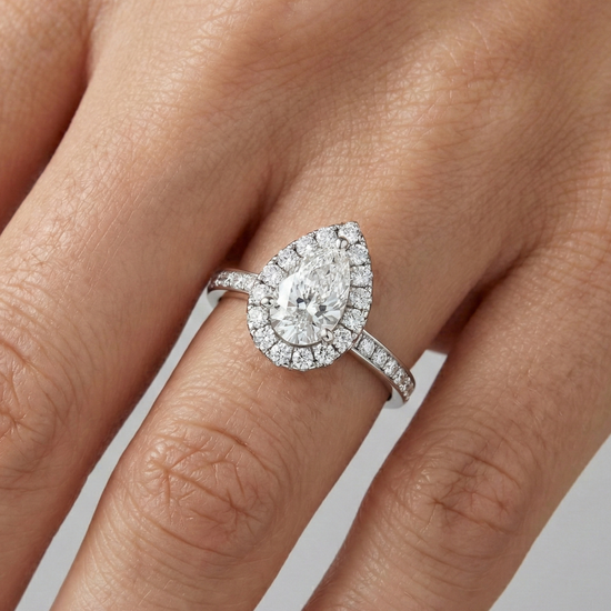 14K white gold pear halo engagement ring worn on hand featuring pear center diamond, round halo and channel set diamond band in cathedral setting.