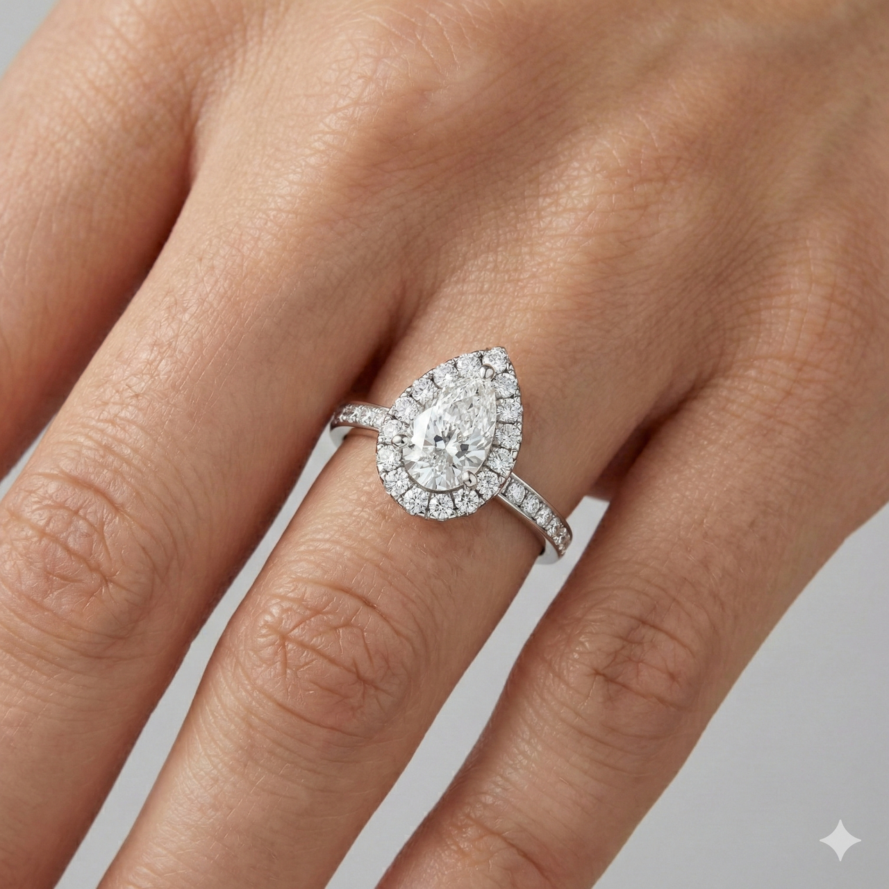 14K white gold pear halo engagement ring worn on hand featuring pear center diamond, round halo and channel set diamond band in cathedral setting.