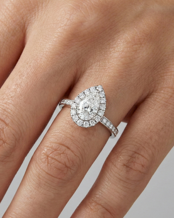 14K white gold pear halo engagement ring worn on hand featuring pear center diamond, round halo and channel set diamond band in cathedral setting.