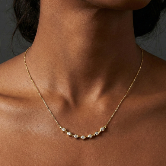 Angled wide view of a yellow gold diamond station necklace resting on a black marble surface, highlighting the contrast between white diamonds and warm gold.