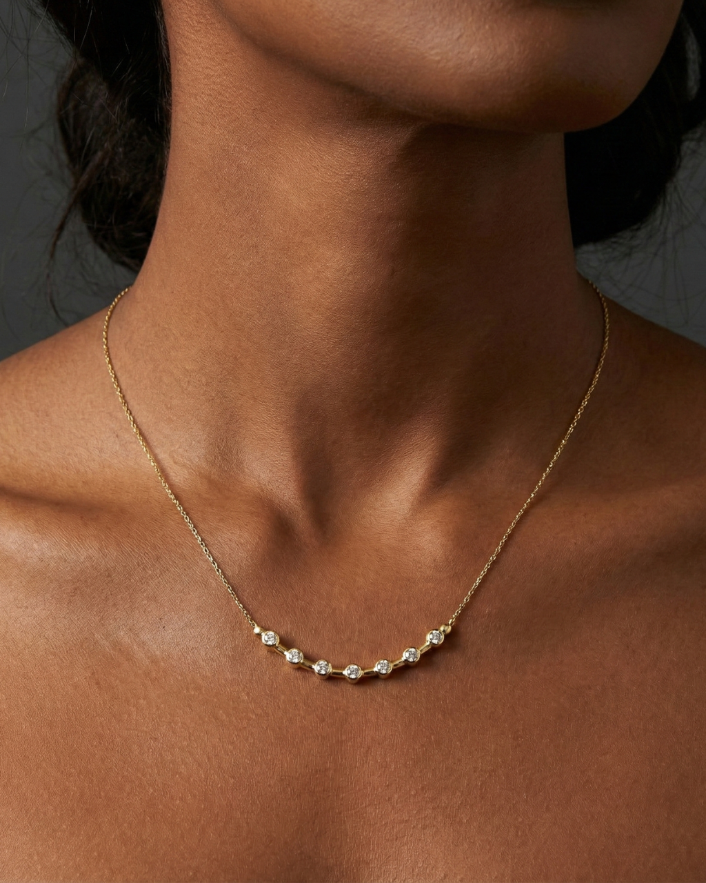 Angled wide view of a yellow gold diamond station necklace resting on a black marble surface, highlighting the contrast between white diamonds and warm gold.