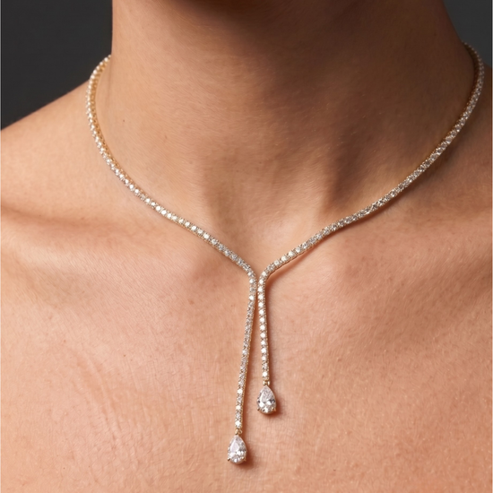 Lifestyle view of a model wearing an elegant 14k yellow gold diamond lariat tennis necklace featuring asymmetric dangling pear-cut diamond drops.
