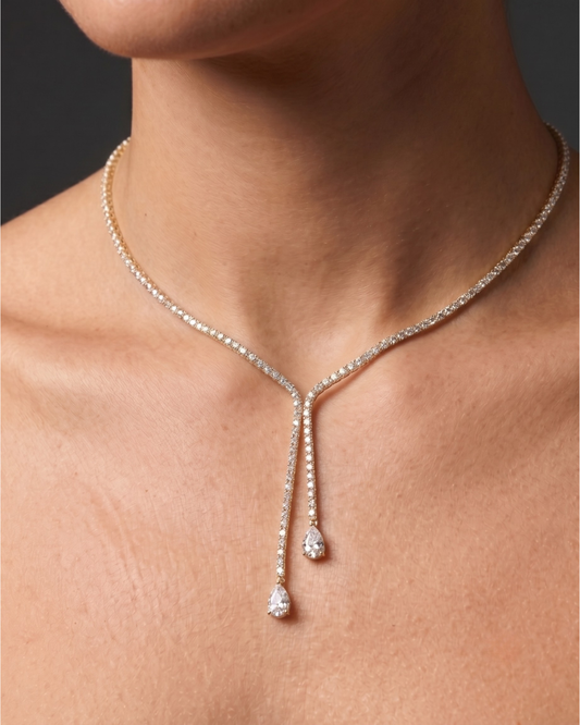 Lifestyle view of a model wearing an elegant 14k yellow gold diamond lariat tennis necklace featuring asymmetric dangling pear-cut diamond drops.