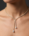 Lifestyle view of a model wearing an elegant 14k yellow gold diamond lariat tennis necklace featuring asymmetric dangling pear-cut diamond drops.