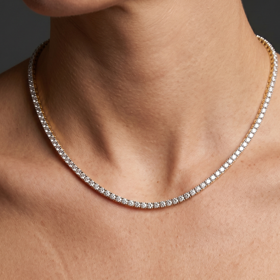 Lifestyle view of a model wearing a delicate 14k yellow gold tennis necklace featuring a thin continuous uniform strand of round-cut white diamonds.