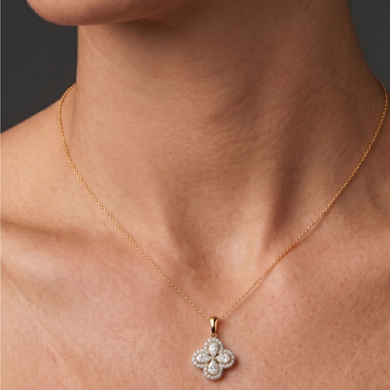 Close-up of a person's neck and collarbone wearing a fine gold chain necklace with a diamond flower pendant featuring pear-shaped stones and a pavé halo.