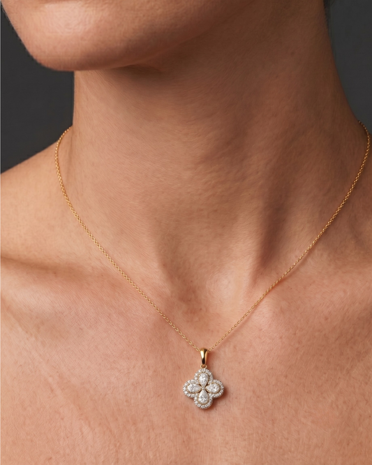 Close-up of a person's neck and collarbone wearing a fine gold chain necklace with a diamond flower pendant featuring pear-shaped stones and a pavé halo.