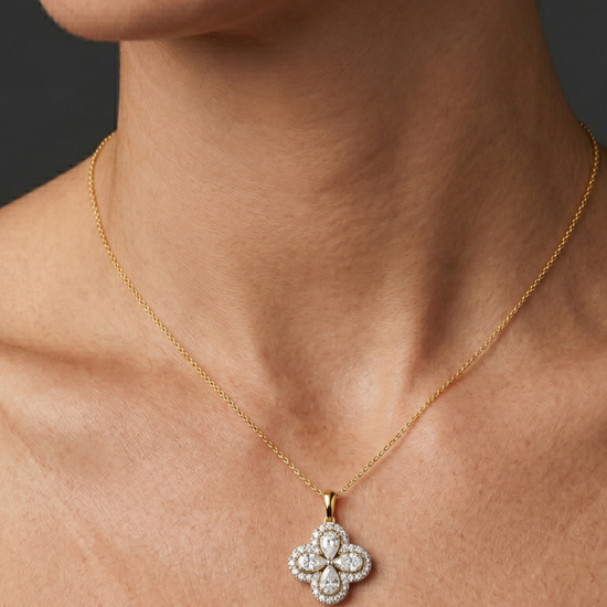 Close-up of a person's neck and collarbone wearing a fine gold chain necklace with a diamond flower pendant featuring pear-shaped stones and a pavé halo.